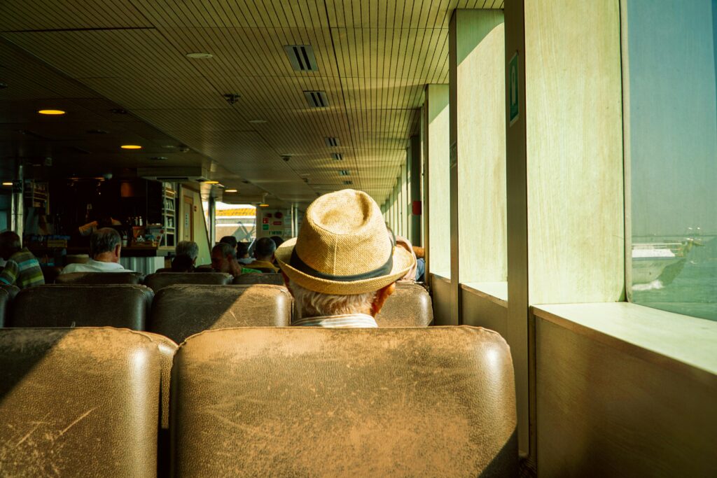 A senior man in a hat sits comfortably on a ferry, enjoying a calm voyage.