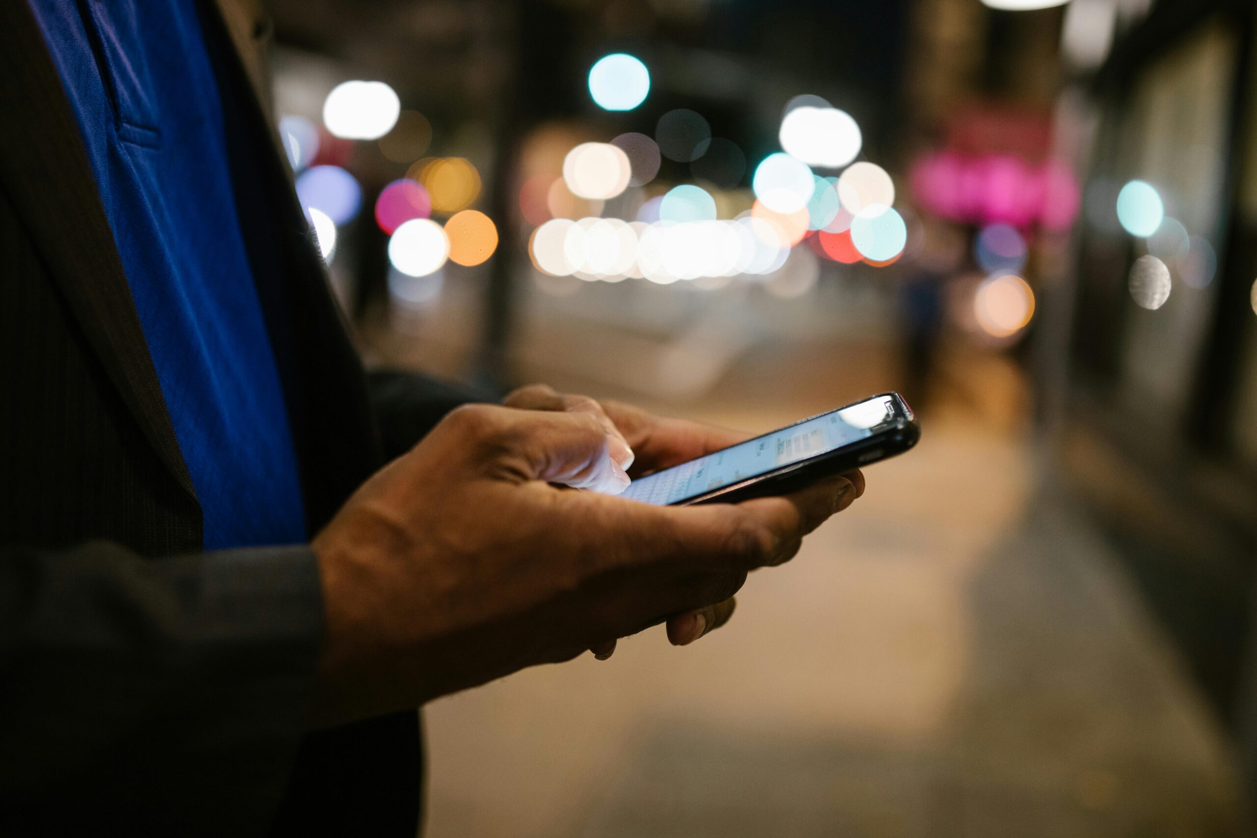 Close-up of a man using a smartphone on a busy city street at night.