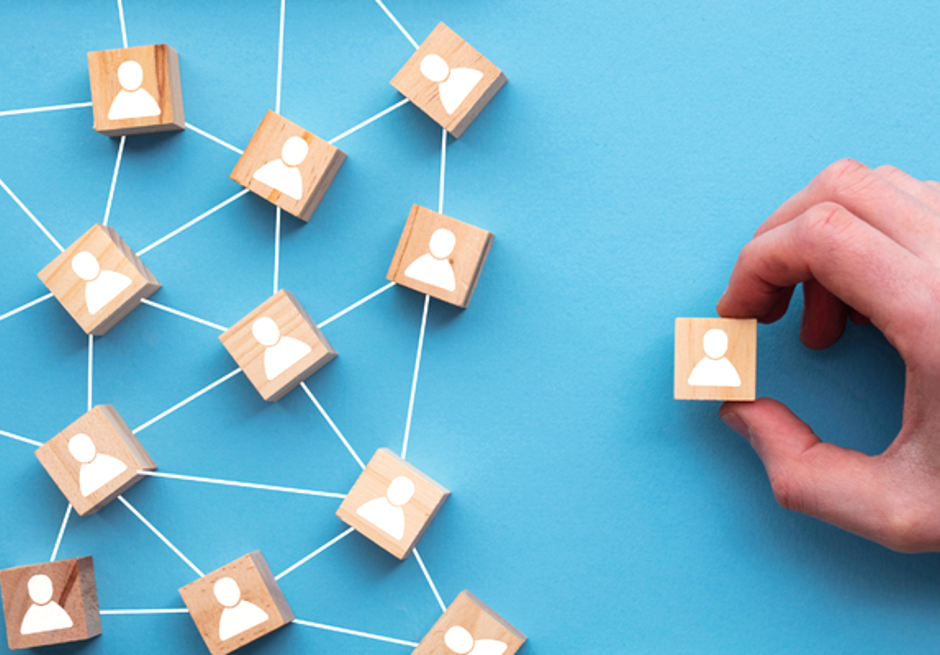 Hand selecting a wooden block with a person icon from a connected network of candidate blocks, representing skills-based hiring and talent acquisition.