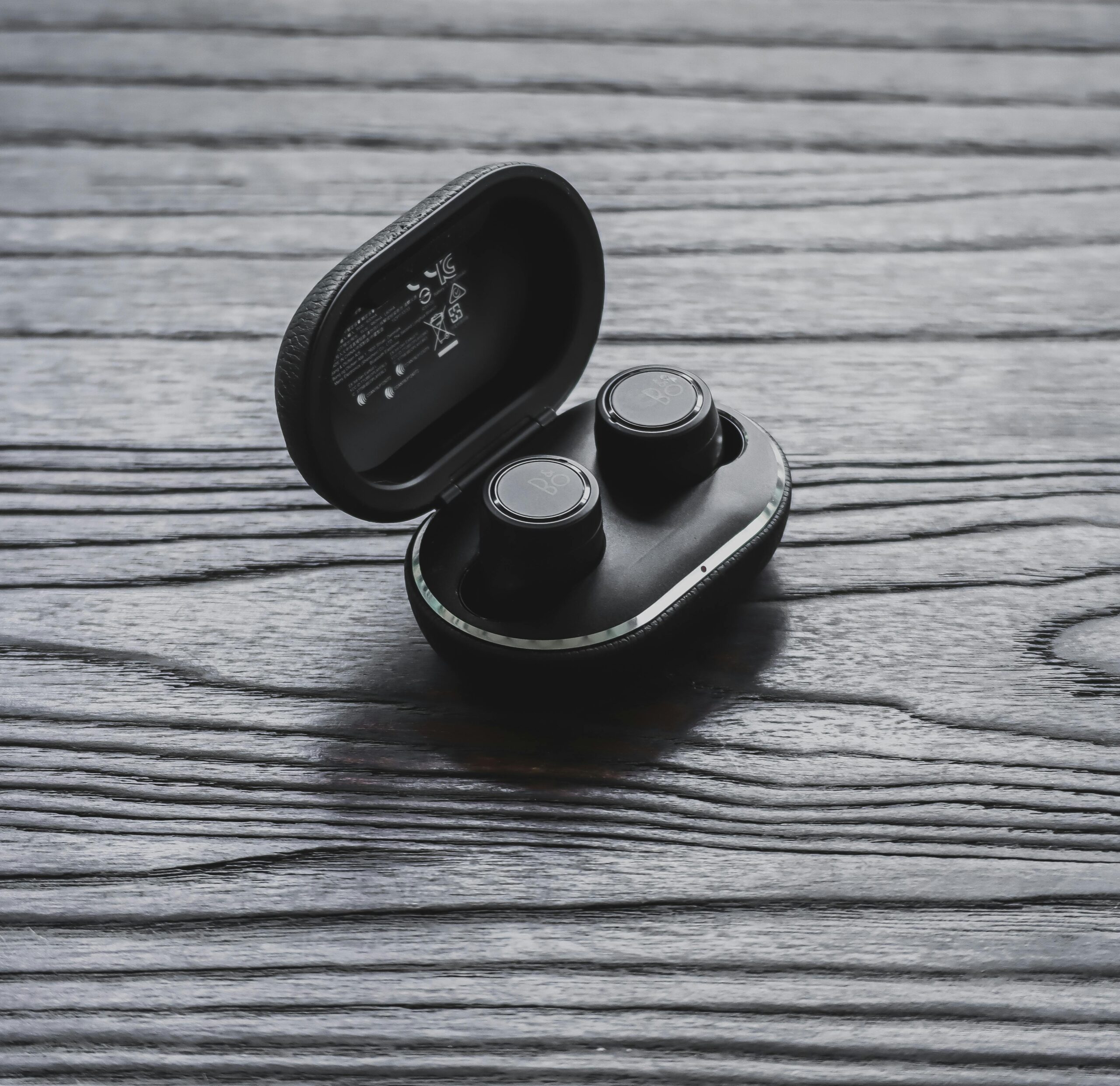 Close-up of true wireless earbuds in an open charging case on a textured wooden surface.