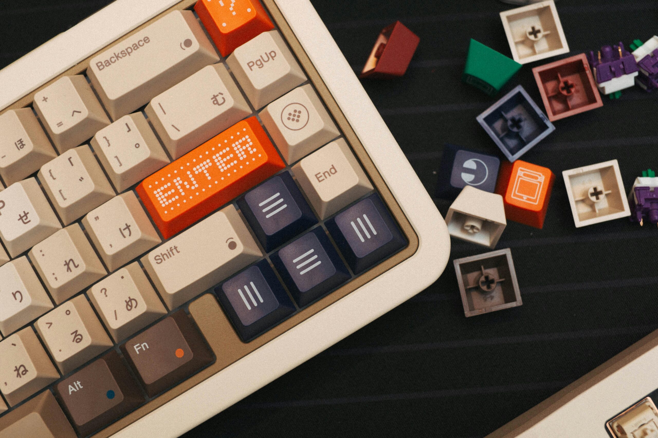 Top view of a beige mechanical keyboard with colorful custom keycaps and loose switches nearby.